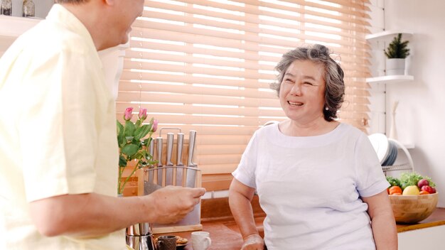 Asiatische ältere Paare, die zu Hause in der Küche frühstücken. Fütterungsplätzchen des chinesischen süßen Paarmanns zu seiner Frau zu Hause.