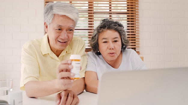 Asiatische ältere Paare unter Verwendung der Laptopkonferenz mit Doktor über Medizininformationen im Wohnzimmer, Paare unter Verwendung der Zeit zusammen beim auf Sofa zu Hause liegen.