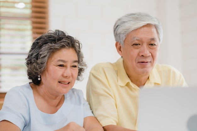 Asiatische ältere Paare unter Verwendung der Laptopkonferenz mit Doktor über Medizininformationen im Wohnzimmer