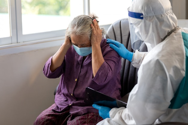 Asiatische ärztin trägt einen psa-anzug. sprechen sie mit einer alten patientin über krankheitssymptome, gesundheitsuntersuchungen bei älteren menschen. sie tragen eine chirurgische maske mit komfort und ermutigung für ältere menschen.