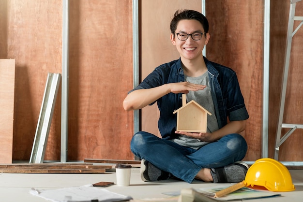 Asiatische attraktive Innenarchitektin mit Brille, die am Baufortschritt der Hausrenovierung mit Lächeln und Selbstvertrauen am Schreibtisch mit Blaupause und Zeichenwerkzeug arbeitet