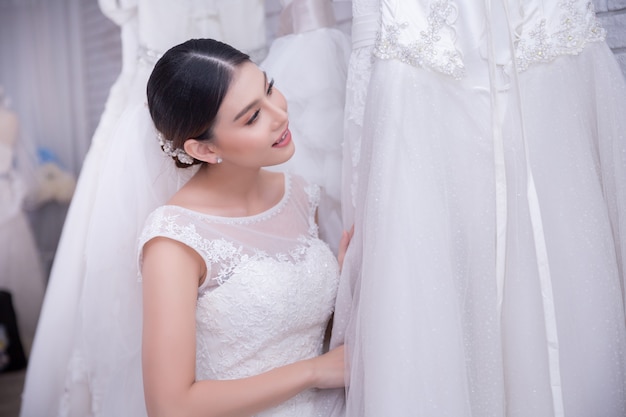 Asiatische Braut der jungen Frau, die auf Hochzeitskleid an der modernen Hochzeit versucht