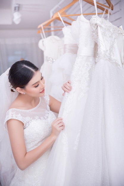 Asiatische Braut der jungen Frau, die auf Hochzeitskleid an der modernen Hochzeit versucht