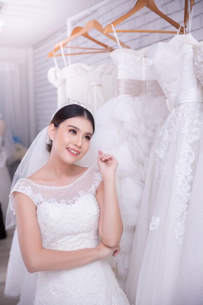 Asiatische Braut der jungen Frau, die auf Hochzeitskleid an der modernen Hochzeit versucht