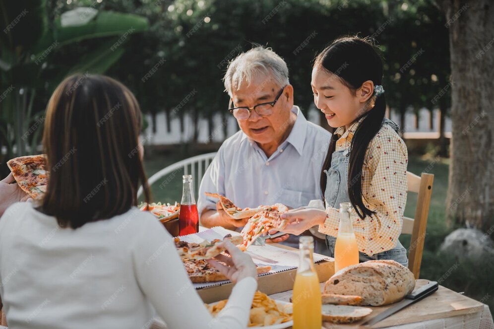 Asiatische familie, die zu hause pizza im garten isst