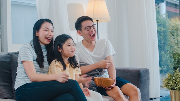 Asiatische familie genießen ihre freizeit entspannen zusammen zu hause. Lebensstilvati, -mutter und -tochter sehen zusammen im Wohnzimmer im modernen Haus nachts fern.