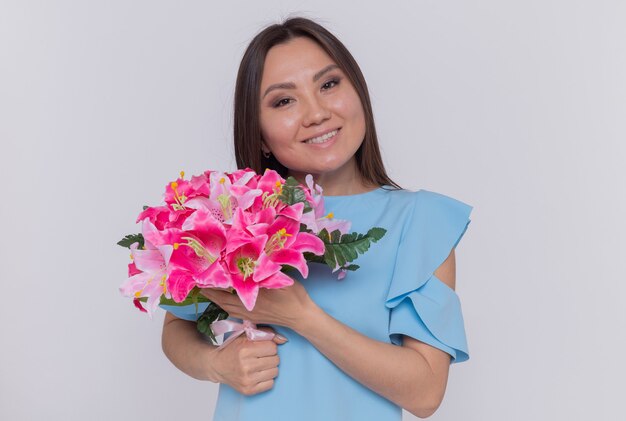 Asiatische Frau, die Blumenstrauß hält, der glücklichen und fröhlichen internationalen Frauentag steht, der über weißer Wand steht