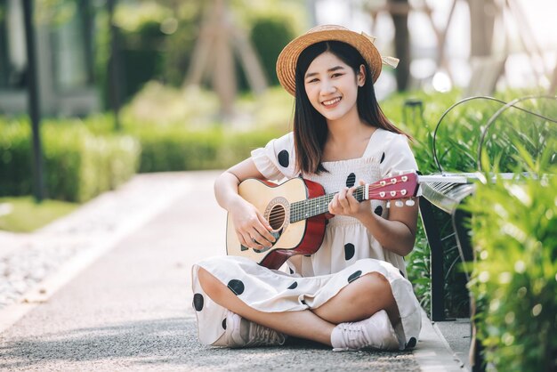 Asiatische Frau, die im Park-Lifestyle- und Erholungskonzept Gitarre spielt