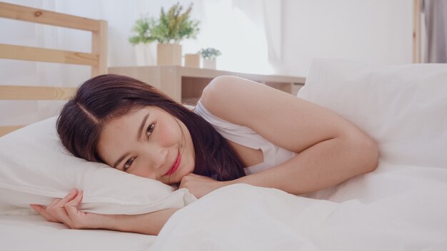 Asiatische Frau, die im Schlafzimmer auf dem Bett liegt, lächelt
