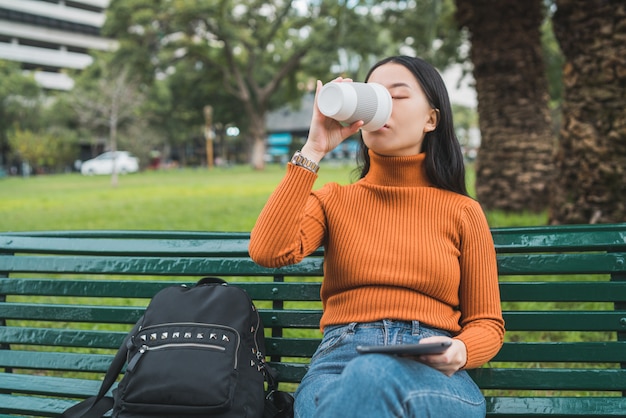 Asiatische Frau, die Kaffee trinkt und eine Tablette verwendet.