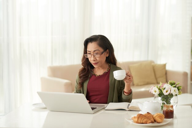 Asiatische Frau, die morgens etwas auf Laptop aufpasst