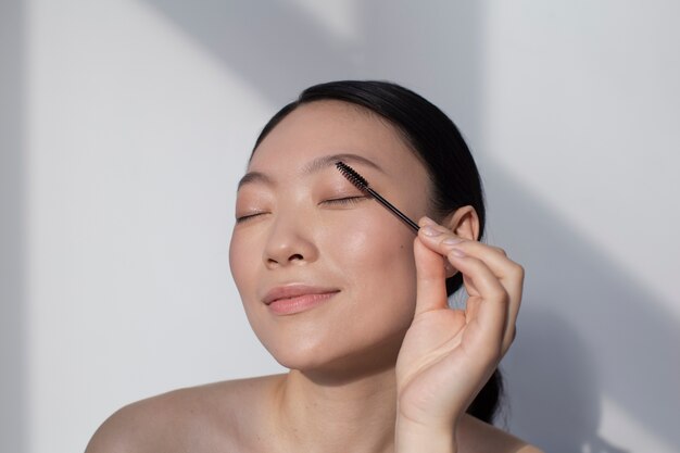 Asiatische Frau, die Wimperntusche aufträgt