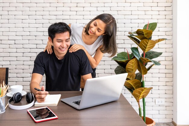 Asiatische Frau Frau motivieren Rat Mann Ehemann Freiberufler arbeiten zu Hause sitzen am Schreibtisch Esstisch im Wohnzimmer