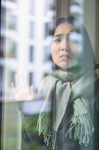 Kostenloses Foto asiatische frau fühlt sich unwohl, bleibt zu hause und schaut mit eifersüchtigem, verzweifeltem gesicht aus dem fenster und will raus