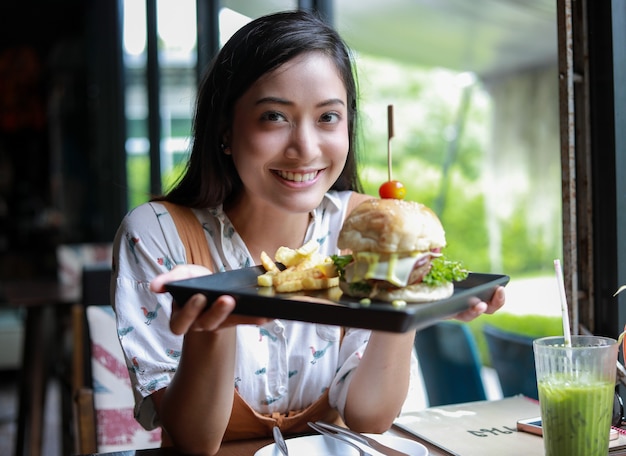 Asiatische frau lächelnd essen hamburger im café