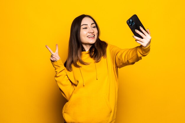 Asiatische Frau macht Selfie-Foto, Videoanruf auf Smartphone an gelber Wand mit Kopierraum