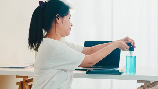 Asiatische Frau mit Alkohol Gel Händedesinfektionsmittel Hand vor offener Tablette zum Schutz Coronavirus waschen. Frauen drücken Alkohol, um für Hygiene zu reinigen, wenn soziale Distanzierung zu Hause bleibt und Selbstquarantänezeit