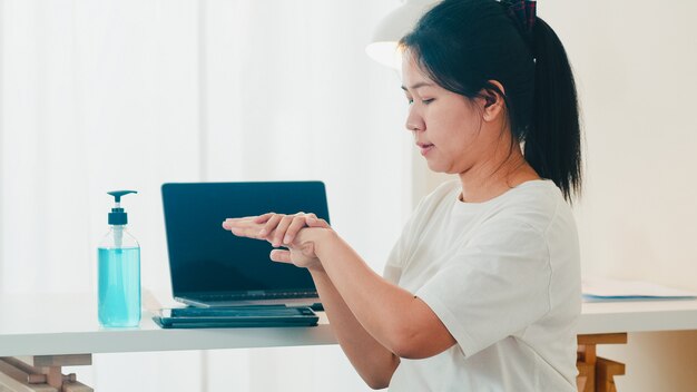 Asiatische Frau mit Alkohol Gel Händedesinfektionsmittel Hand vor offener Tablette zum Schutz Coronavirus waschen. Frauen drücken Alkohol, um für Hygiene zu reinigen, wenn soziale Distanzierung zu Hause bleibt und Selbstquarantänezeit