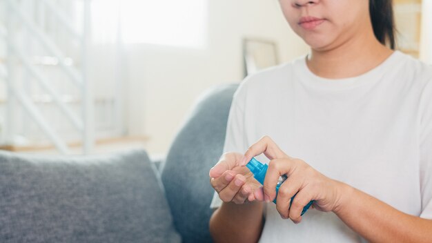 Asiatische Frau mit Alkoholspray Händedesinfektionsmittel waschen Hand zum Schutz des Coronavirus. Frau sitzt am Sofa saubere Hand für Hygiene, wenn soziale Distanzierung zu Hause bleibt und Selbstquarantänezeit.