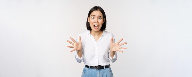 Asiatische Frau schaut in die Kamera und schreit in Panik Junges koreanisches Mädchen, das ängstlich panisch aussieht, die Hände schüttelt und über weißem Hintergrund schreit