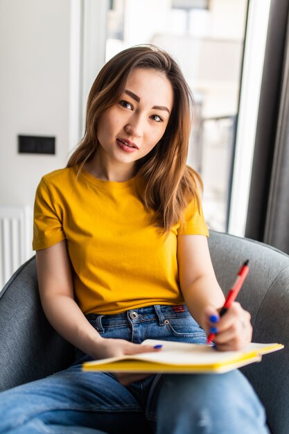 Asiatische Frau schreibt in Notizblock auf weißem modernen Stuhl