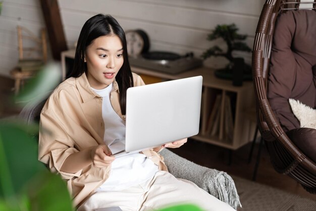 Asiatische Frau sieht aufgeregt und erstaunt aus, als sie den Laptop-Bildschirm gewinnt, der online zu Hause sitzt