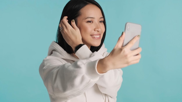 Asiatische Frauen tragen Hoodie Putzen und Selfie auf dem Smartphone über farbigen Hintergrund Moderne Technologie Schöne Frau posiert im Studio