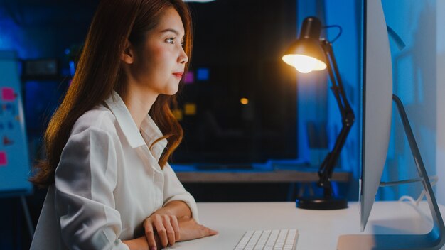 Asiatische Geschäftsfrau, die Computer verwendet, spricht mit Kollegen über Plan in Videoanruf, während sie nachts von zu Hause im Wohnzimmer arbeiten. Selbstisolation, soziale Distanzierung, Quarantäne zur Vorbeugung von Coronaviren.