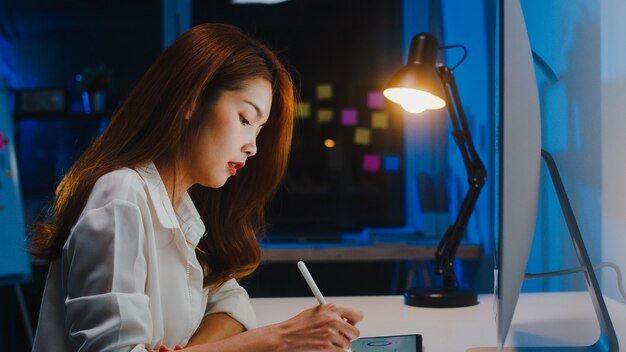 Asiatische Geschäftsfrau, die Computer verwendet, spricht mit Kollegen über Plan in Videoanruf, während sie nachts von zu Hause im Wohnzimmer arbeiten. Selbstisolation, soziale Distanzierung, Quarantäne zur Vorbeugung von Coronaviren.