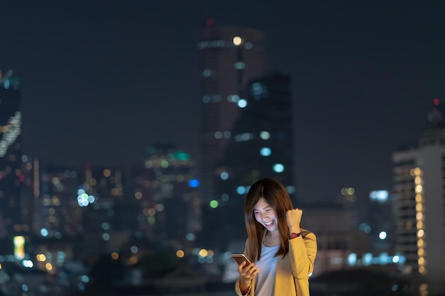 Asiatische geschäftsfrau, die intelligentes mobiltelefon mit lächelnaktion verwendet