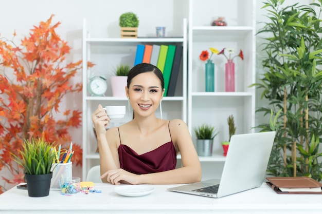 Asiatische Geschäftsfrau machen eine Kaffeepause, nachdem sie an der Laptop-Computer auf Schreibtisch gearbeitet hat