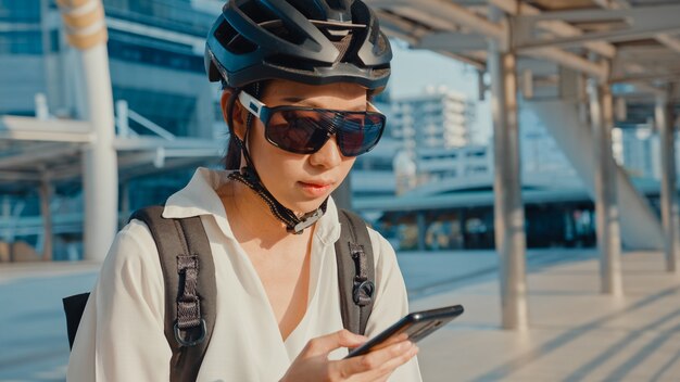 asiatische Geschäftsfrau mit Rucksack mit Handy in der Stadtstraße gehen zur Arbeit im Büro.