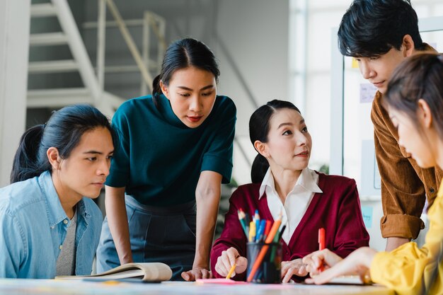 Asiatische Geschäftsleute und Geschäftsfrauen treffen sich mit Brainstorming-Ideen über kreative Webdesign-Planungsanwendungen und entwickeln ein Vorlagenlayout für ein Mobiltelefonprojekt, das in einem kleinen Büro zusammenarbeitet.