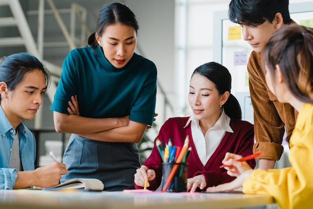 Asiatische Geschäftsleute und Geschäftsfrauen treffen sich mit Brainstorming-Ideen über kreative Webdesign-Planungsanwendungen und entwickeln ein Vorlagenlayout für ein Mobiltelefonprojekt, das in einem kleinen Büro zusammenarbeitet.