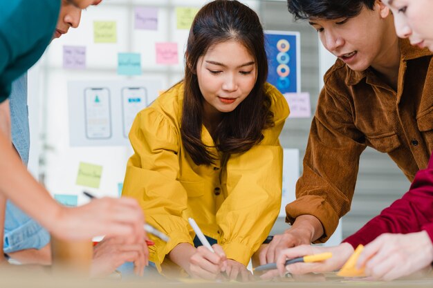 Asiatische Geschäftsleute und Geschäftsfrauen treffen sich mit Brainstorming-Ideen über kreative Webdesign-Planungsanwendungen und entwickeln ein Vorlagenlayout für ein Mobiltelefonprojekt, das in einem kleinen Büro zusammenarbeitet.