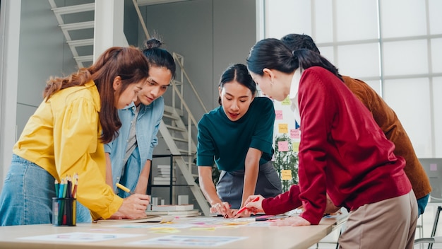 Asiatische Geschäftsleute und Geschäftsfrauen treffen sich mit Brainstorming-Ideen über kreative Webdesign-Planungsanwendungen und entwickeln ein Vorlagenlayout für ein Mobiltelefonprojekt, das in einem kleinen Büro zusammenarbeitet.