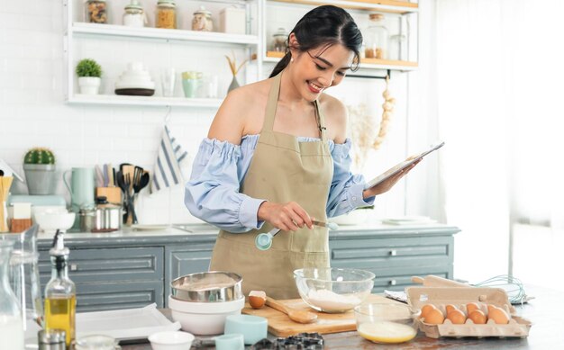 Asiatische Hausfrau in der Küche mit Tablet für die Online-Suche nach Rezepten, die die Bäckerei hausgemacht kochen