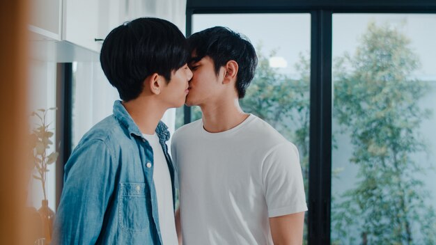 Asiatische homosexuelle Paare, die zu Hause Raum stehen und umarmen. Die jungen hübschen LGBTQ + Männer, die glücklich küssen, entspannen sich Rest verbringen zusammen romantische Zeit in der modernen Küche am Haus morgens.