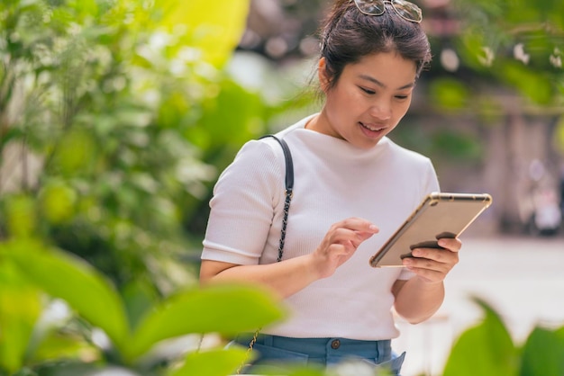 Asiatische junge Erwachsene der digitalen Nomadin, die überall Kommunikationshand unter Verwendung des Tablet-Online-Kontakts arbeiten und sich mit neuem Lebensstil fröhlichem Glück im Caféparkgarten treffen, konzentrieren sich auf die Arbeit