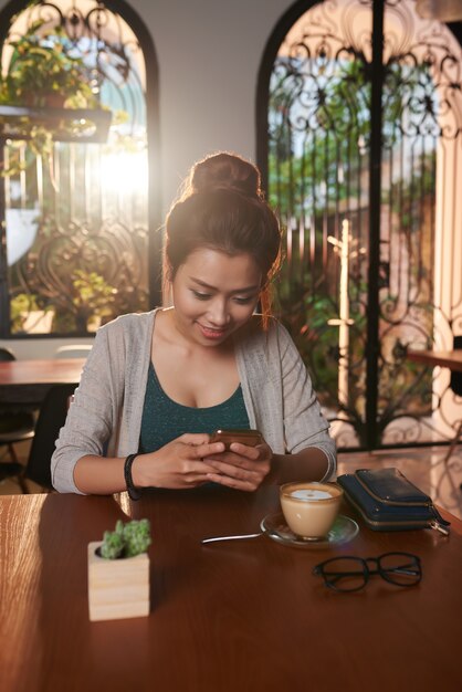 Asiatische junge Frau, die im Café simst