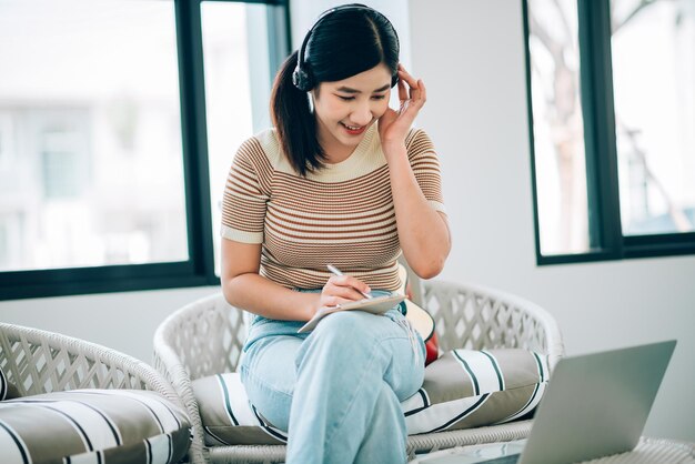 Asiatische junge Frau, die Laptop verwendet, um von zu Hause aus im Wohnzimmer zu arbeiten