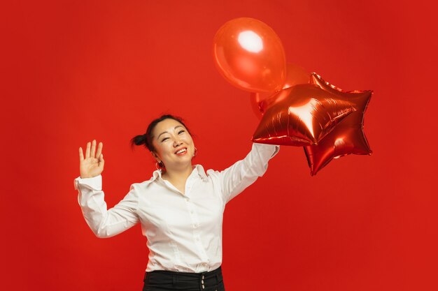 Asiatische junge Frau, die Luftballons an der roten Wand hält