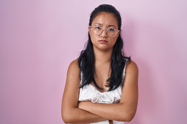 Kostenloses Foto asiatische junge frau, die über rosa hintergrund steht, skeptisch und nervös, missbilligender gesichtsausdruck mit verschränkten armen. negativer mensch.