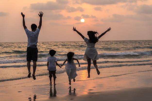 Asiatische junge glückliche Familie genießen abends Urlaub am Strand. Vater, Mutter und Kind entspannen sich beim Laufen in der Nähe des Meeres, während Silhouette Sonnenuntergang. Lifestyle Reise Urlaub Urlaub Sommer Konzept.