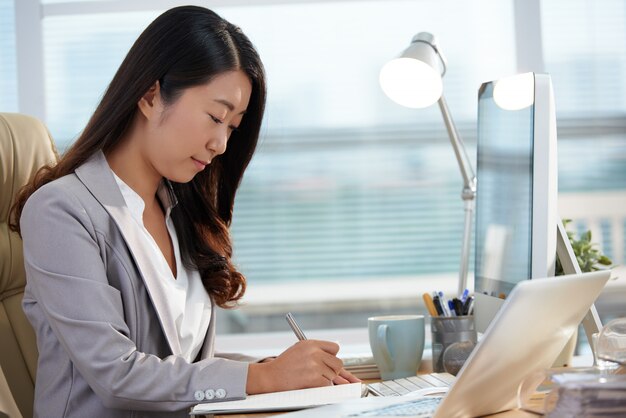 Asiatische Karrierefrau, die am Schreibtisch im Büro sitzt und mit Dokumenten arbeitet