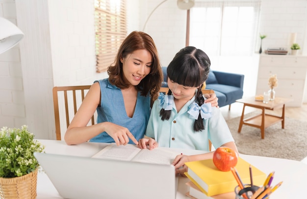 Asiatische kleine junge Studentin der Schule, die lernt, auf Tisch zu sitzen und mit seiner Mutter zu Hause arbeitet.