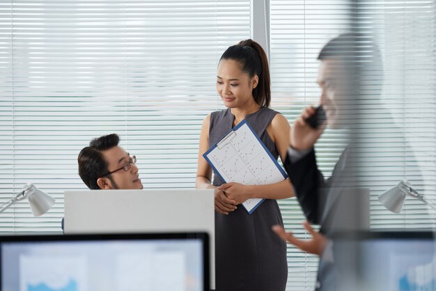 Asiatische Mitarbeiter, die etwas während ihr Kollege spricht am Telefon besprechen