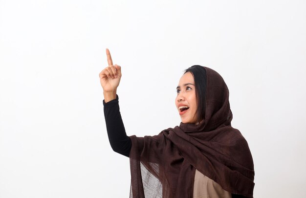 Asiatische muslimische frau auf einem schleier oder hijab, die lächelt und auf leeren raum blickt, während sie auf etwas zeigt