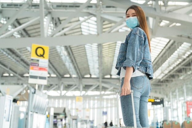 Asiatische reisende lässige kleidung tragen gesichtsmaske schutz handzug gepäck im airoirt abflugterminal sicherheitsreisekonzept