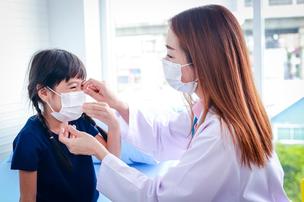 Asiatische schöne ärztin, die einem süßen kleinen mädchen eine weiße maske trägt. das konzept der medizinischen dienste in krankenhäusern, gesundheitschecks für kleine kinder.
